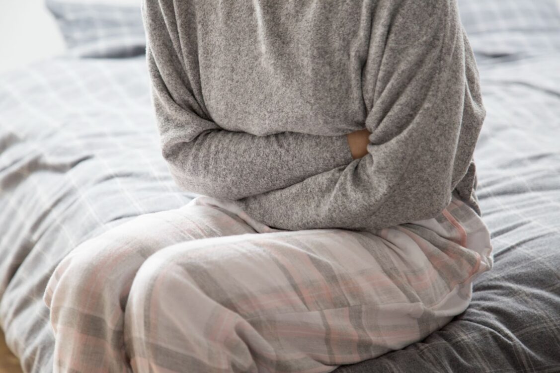 Close up of sick woman on bed keeping hands on stomach