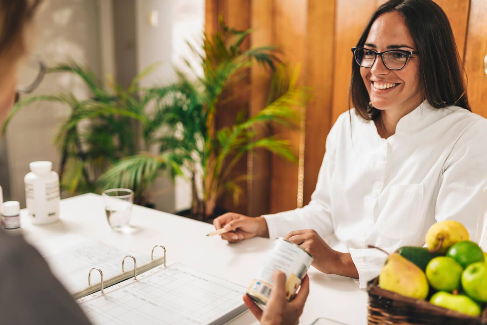 a smiling woman sitting at a table, a dish of apples next to her