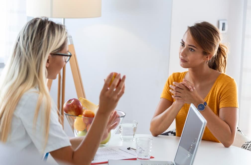 Two women discussing over a bowl of fruit, possibly a nutrition consultation