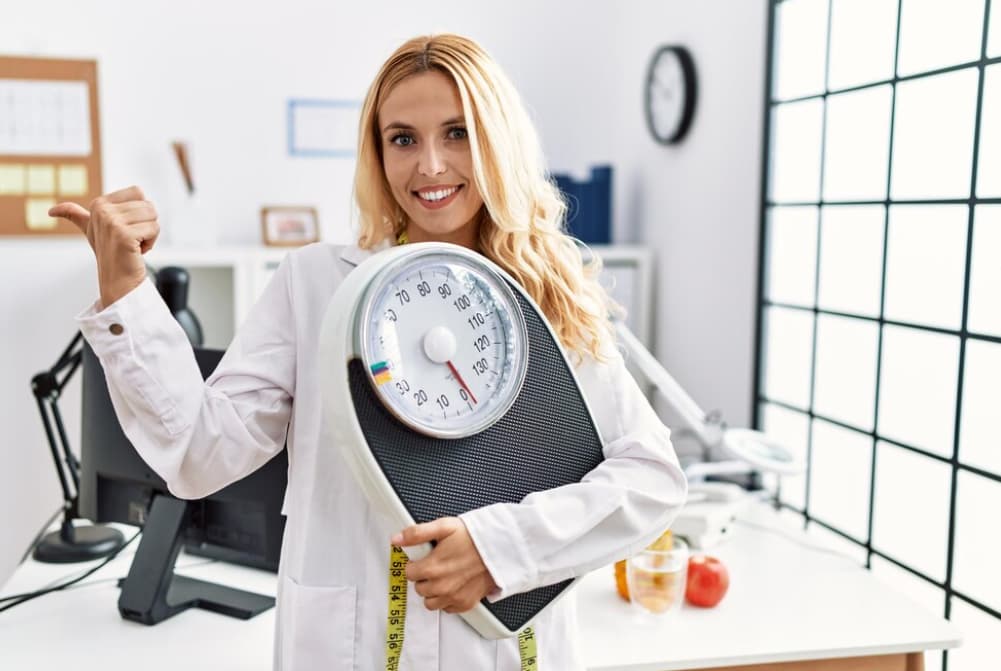 A smiling dietitian holding a scale and tape measure, indicating weight management